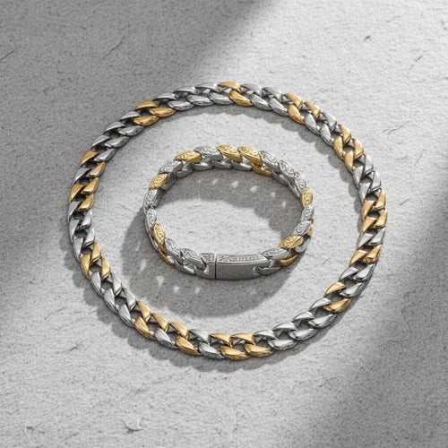 Two silver and gold chain necklaces on a textured gray surface.  Curb Vine Men&