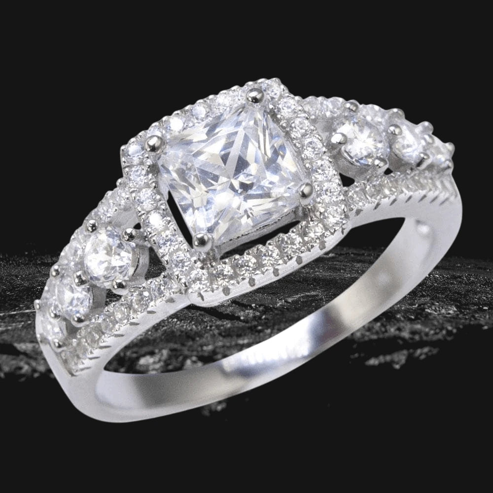 Aria Ring for female featuring a sterling silver band with rhodium plating and a large square-cut center stone surrounded by smaller sparkling stones in an elegant design.