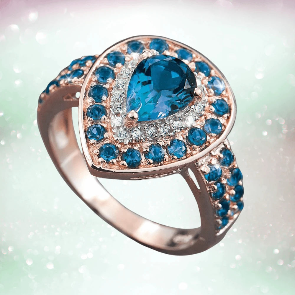 Encantada Ring in sterling silver with rose gold plating, featuring a pear-shaped blue gemstone surrounded by smaller blue and clear stones, elegant women's jewelry.