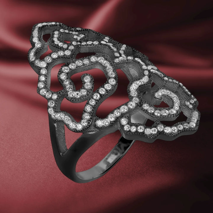Desert Rose Black Ring crafted from sterling silver with an intricate openwork floral design adorned with sparkling clear stones, displayed on a rich burgundy fabric background.