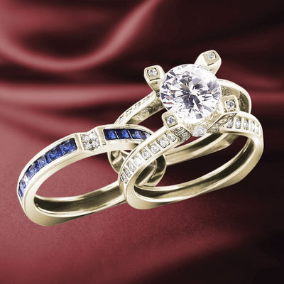 Natalia Gold Ring featuring a large round center stone set in gold-plated sterling silver, accompanied by two complementary rings with blue and clear stones on a rich burgundy background.