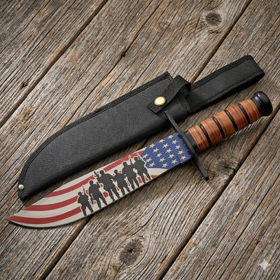 Freedom Fighter Bowie Knife featuring an American flag design blade with soldier silhouettes and a leather-wrapped handle resting on a wooden surface beside a black sheath.