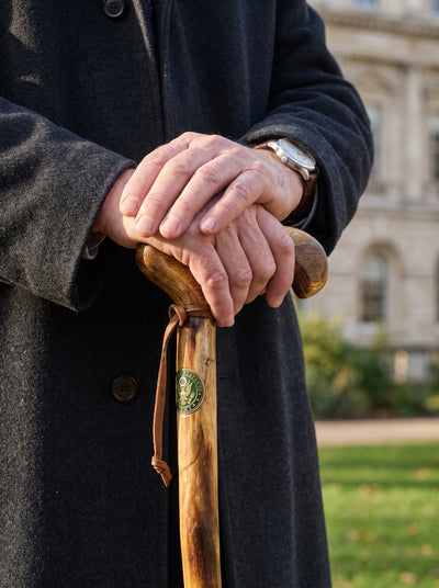 Army Veterans Walking Cane held by a person in a dark coat showing polished wood grain and a leather wrist strap Up To 75% Off Retail