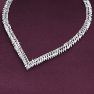 Sparkling necklace with layered rows of clear stones and repeating leaf-shaped details arranged in a V curve against a deep plum background