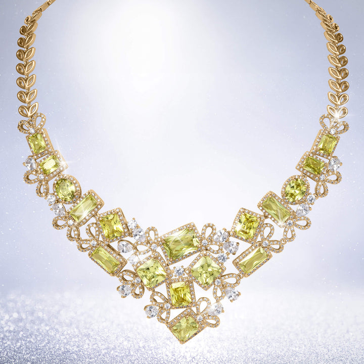 Ornate gold necklace with vibrant green gemstones and sparkling clear stones arranged in an elaborate bib design against a softly shimmering background