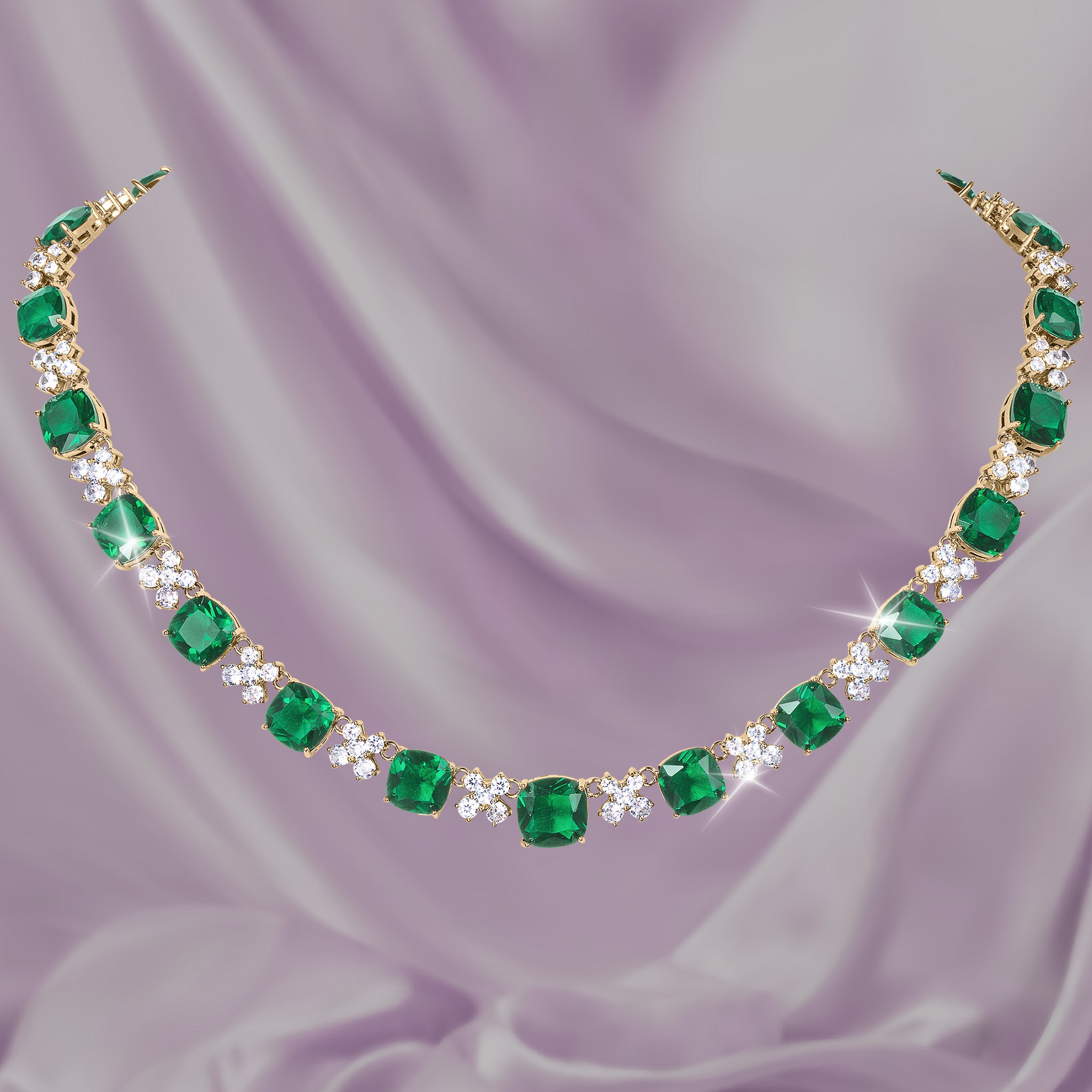 Freya Necklace with vibrant emerald green gemstones clear crystal accents and a gold tone setting displayed on soft lavender fabric Up To 75% Off Retail