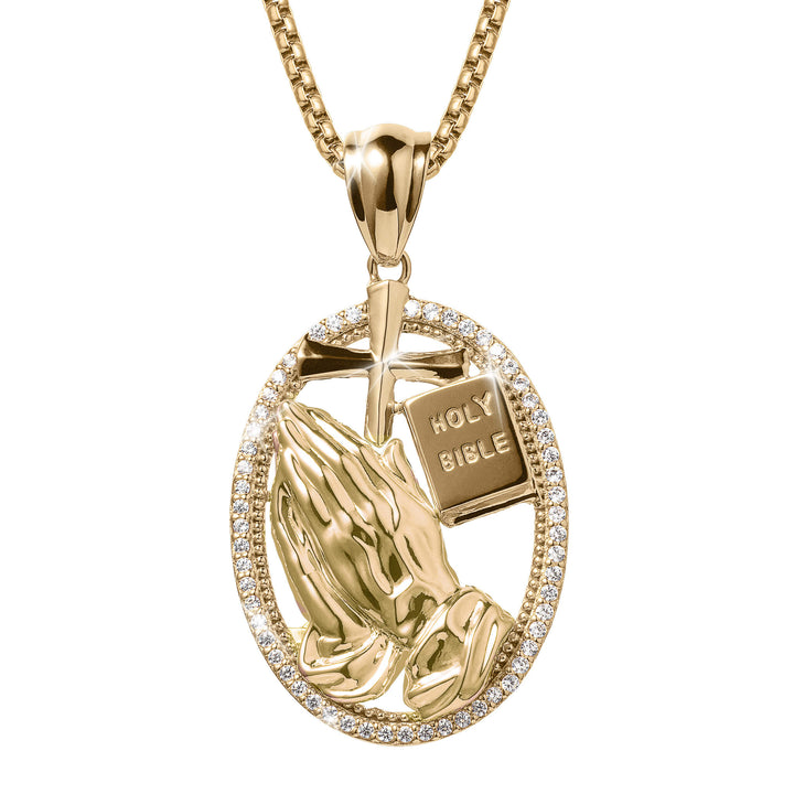 Holy Pendant featuring gold praying hands, a cross, and a small Holy Bible surrounded by a sparkling stone-studded oval frame on a gold chain necklace.