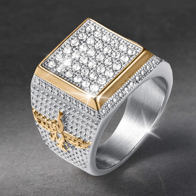 Two tone silver and gold ring with a square top covered in clear stones and a detailed gold emblem on the textured band