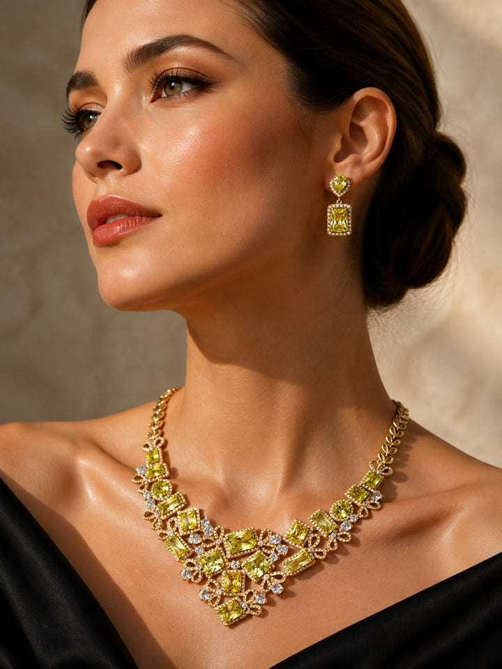 Golden Willow Collection Set featuring a woman wearing an ornate gold necklace and matching drop earrings with sparkling green and clear accents Up To 75% Off Retail