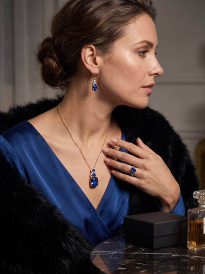 Elara Sapphire Pendant worn with matching blue sapphire earrings and ring by an elegant woman in a blue dress and black fur wrap