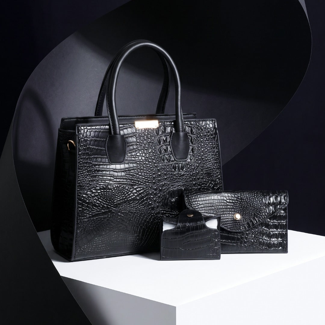 A black crocodile-embossed leather handbag set displayed on a white pedestal against a dark studio background. The set includes a structured tote bag with dual top handles, a matching zip-around wallet, and a small rectangular card case. Gabriella Bag Collection featuring a black crocodile texture handbag wallet and mini purse with polished gold accents Up To 75% Off Retail