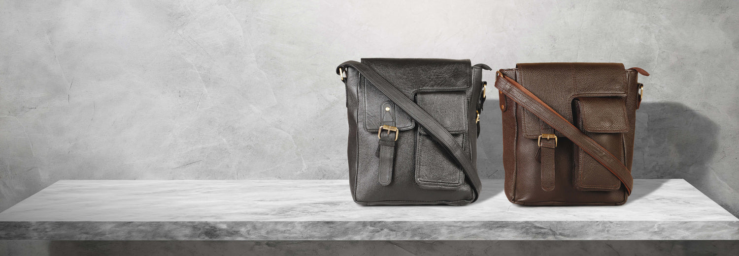 Two leather crossbody messenger bags in black and brown displayed on a white marble shelf against a textured gray background
